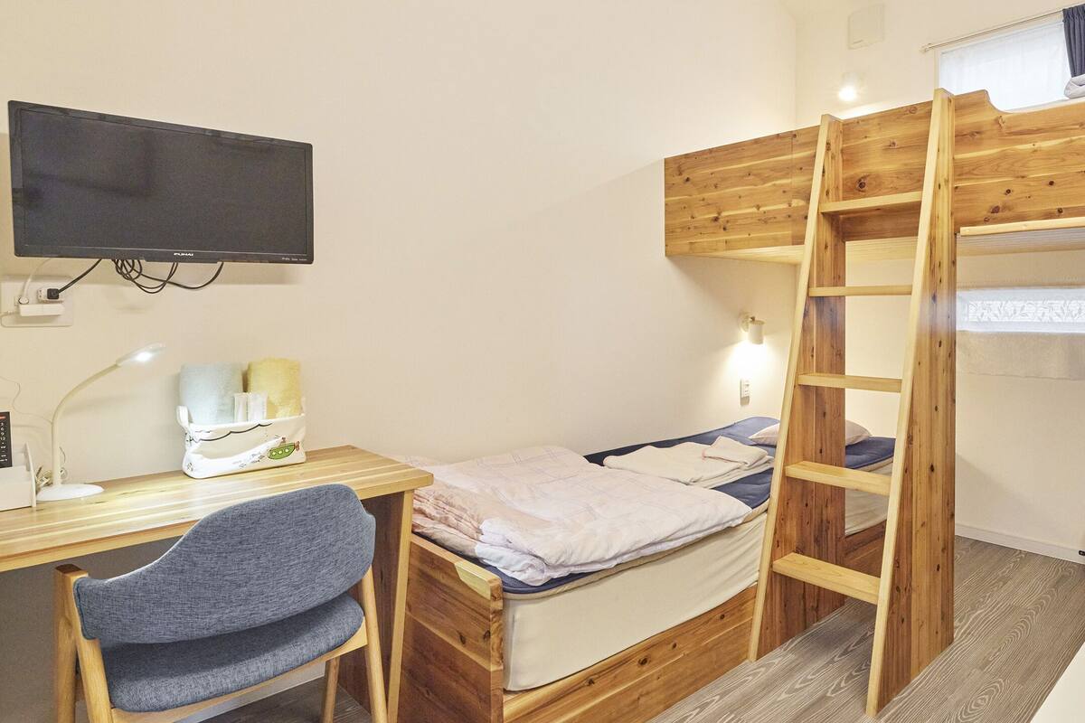 Een stapelbed met een houten ladder, een bureau met een computer en lamp, en een stoel.
