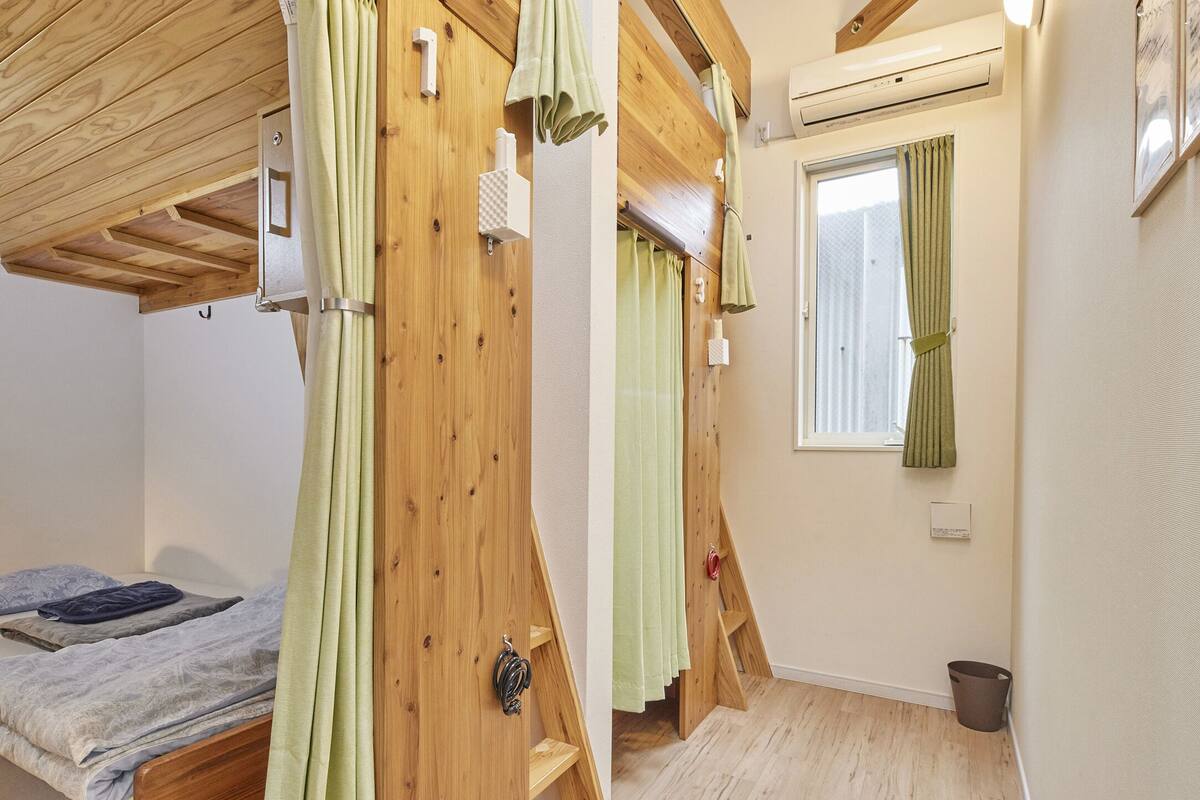 Een slaapkamer met een houten plafond, een bed met een grijze matras en een raam met groene gordijnen.