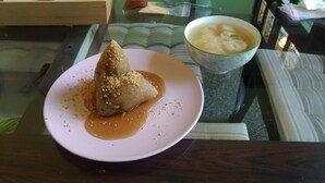 Ein Teller mit einer dreieckigen Speise und einer Schüssel Suppe auf einem Glastisch.