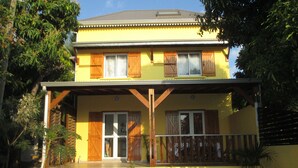A two-story building with a balcony, wooden shutters, and potted plants.