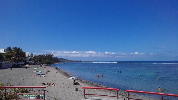 A beach with people swimming and sunbathing, a clear sky, and a distant shoreline.