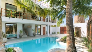 Una casa de dos pisos con piscina, palmeras y una escalera que conduce al nivel superior.
