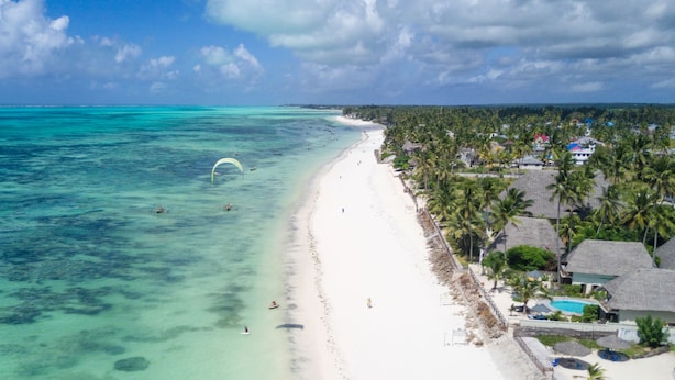 Un resort en la playa con una orilla de arena blanca, aguas turquesas cristalinas y una hilera de bungalows con techo de paja.