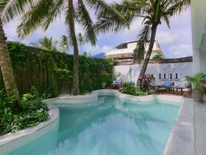 A swimming pool with a curved edge, surrounded by lush greenery and palm trees. There are lounge chairs and a sign for 'Lulu Zanzibar Apartments'. - UVIVU by Jambiani Villas (Jambiani)