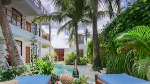 Un área exterior tropical con piscina, terraza de madera y sillas de descanso.
