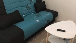 Una sala moderna con un sofá azul y negro, una mesita blanca y dos estanterías con libros y adornos.