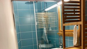 Un baño con cabina de ducha de vidrio, un lavamanos blanco y un estante de madera.