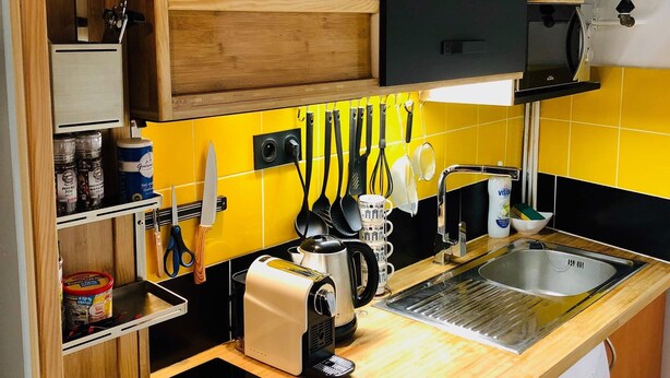 Una cocina compacta con lavadora integrada, cafetera y hervidor.