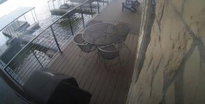 A deck with a round table and chairs, a grill, and a railing overlooking water.
