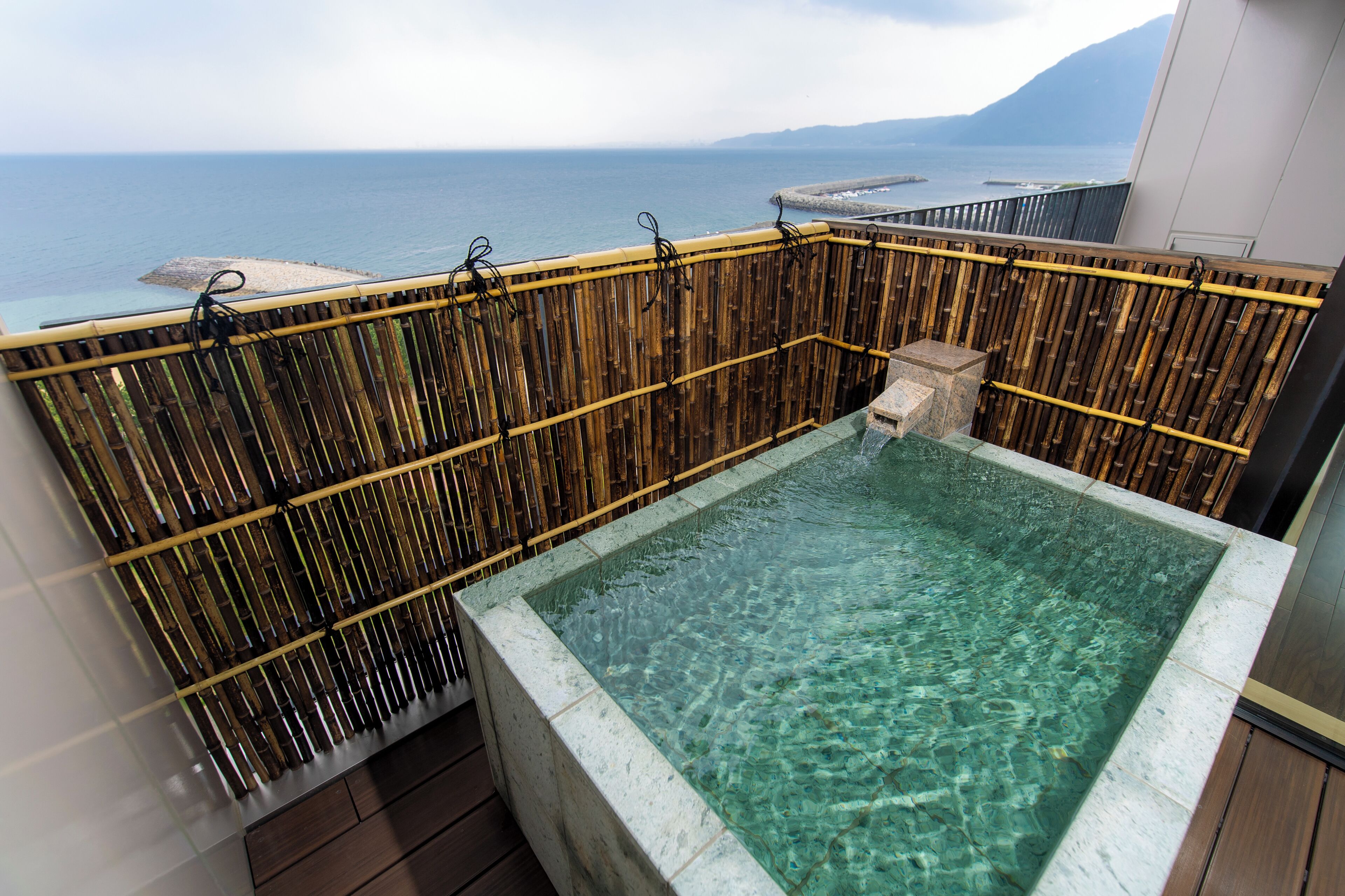 A clear pool with a bamboo fence, a stone structure, and a view of the sea.