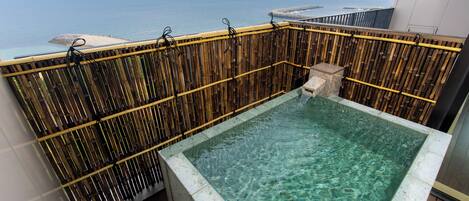 A clear pool with a bamboo fence, a stone structure, and a view of the sea.