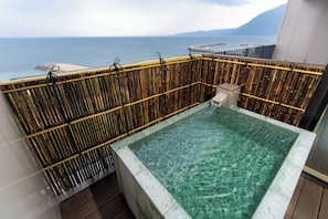 A clear pool with a bamboo fence, a stone structure, and a view of the sea. - REX HOTELBeppu (Beppu)