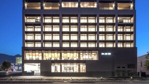 A multi-story building with a modern architectural design, featuring a ground-level entrance with glass doors and a visible seating area. - REX HOTELBeppu (Beppu)
