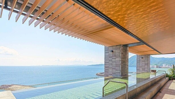 A modern infinity pool with clear water, a wooden pergola, and a view of the sea and distant mountains. - REX HOTELBeppu (Beppu)
