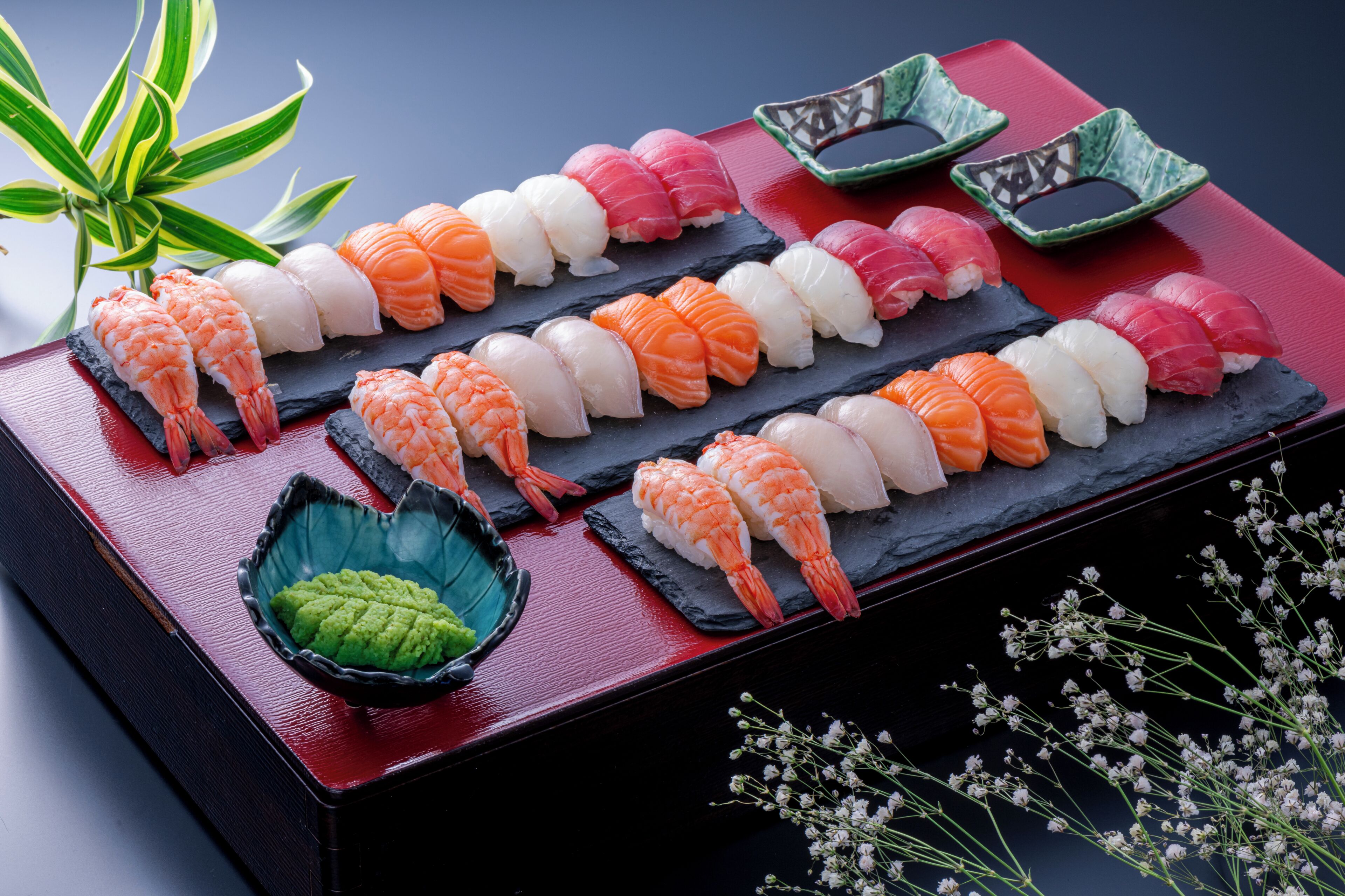 A variety of sushi arranged on a black slate plate with a red background.