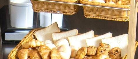 A breakfast buffet with various breads, pastries, and rolls displayed in wicker baskets.
