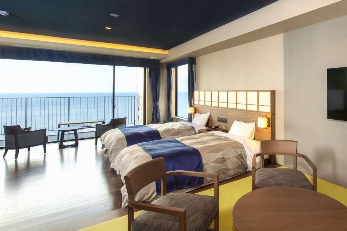 A hotel room with a large bed, two bedside tables, a desk, and chairs. The room has a view of the ocean.