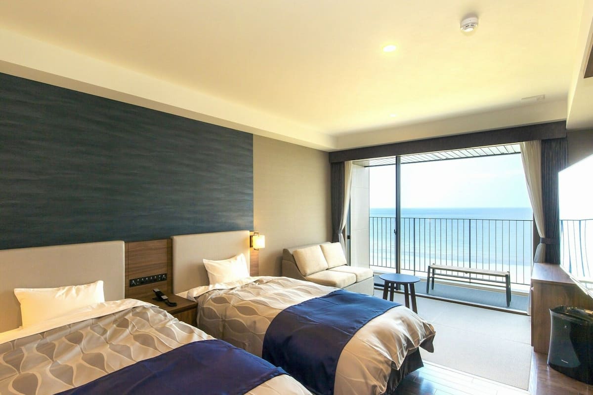 A hotel room with two beds, a balcony with a view of the sea, and a small table.