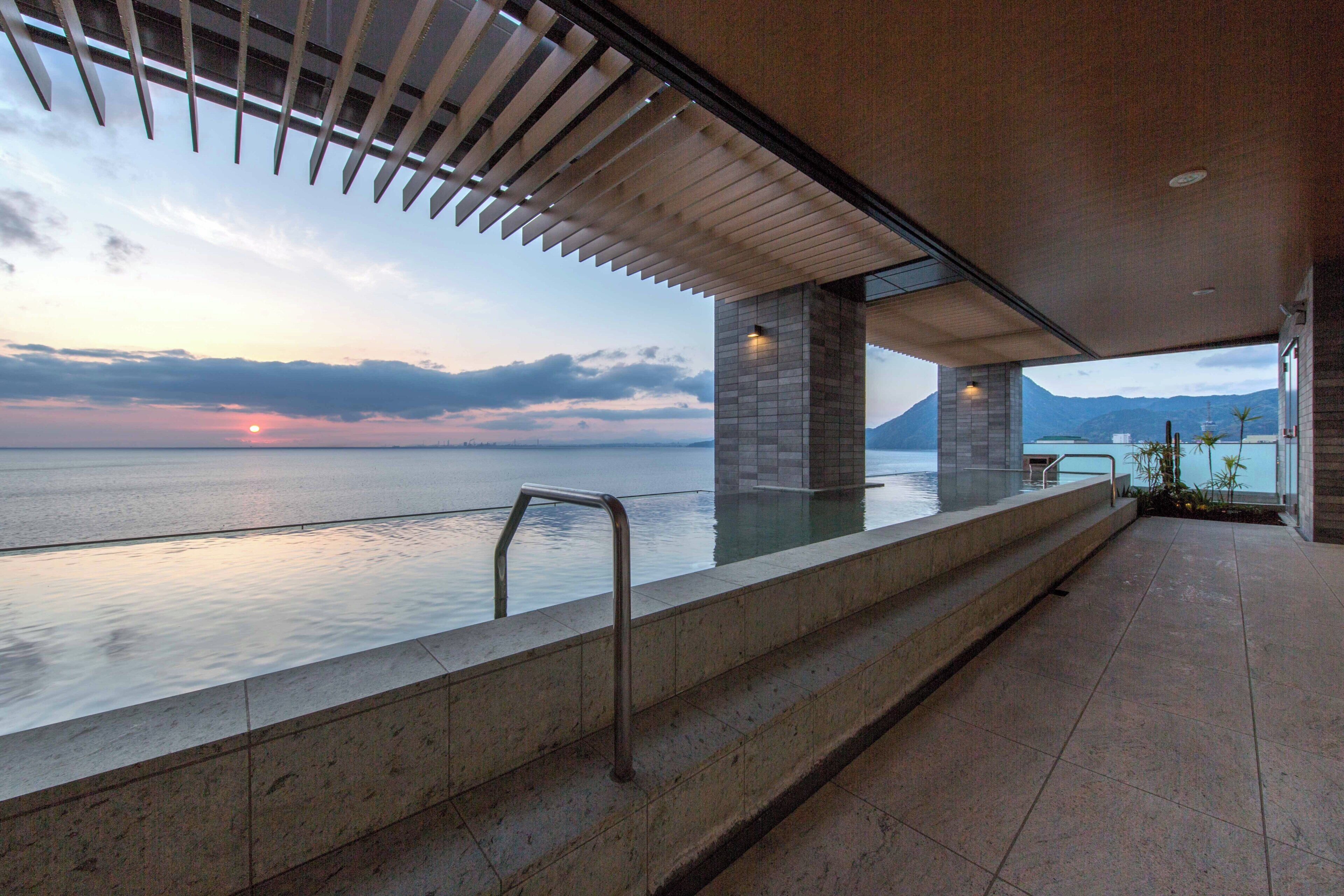 A modern outdoor pool area with a view of the sea and mountains.