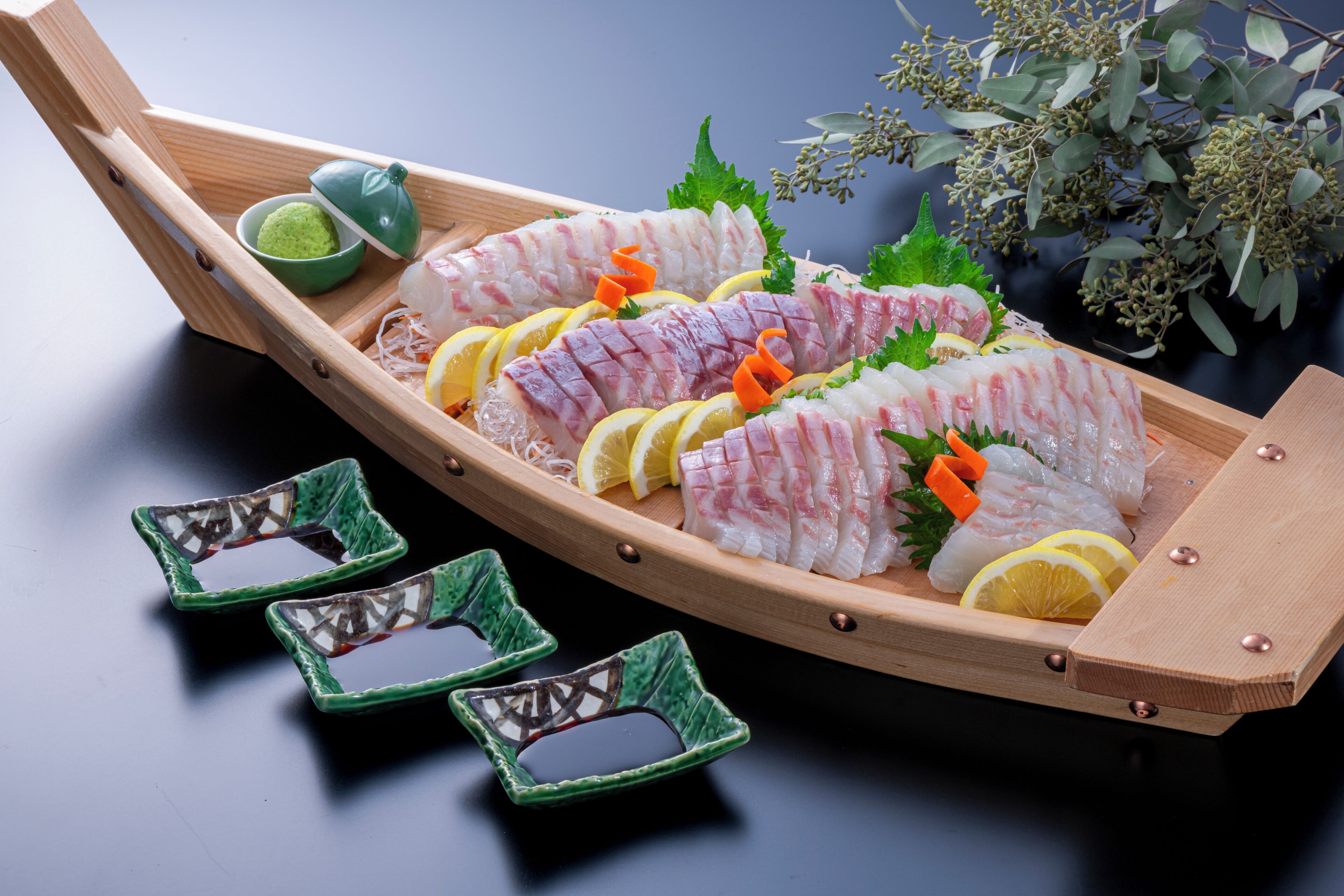 Un plato con forma de barco de madera con sashimi y guarniciones.
