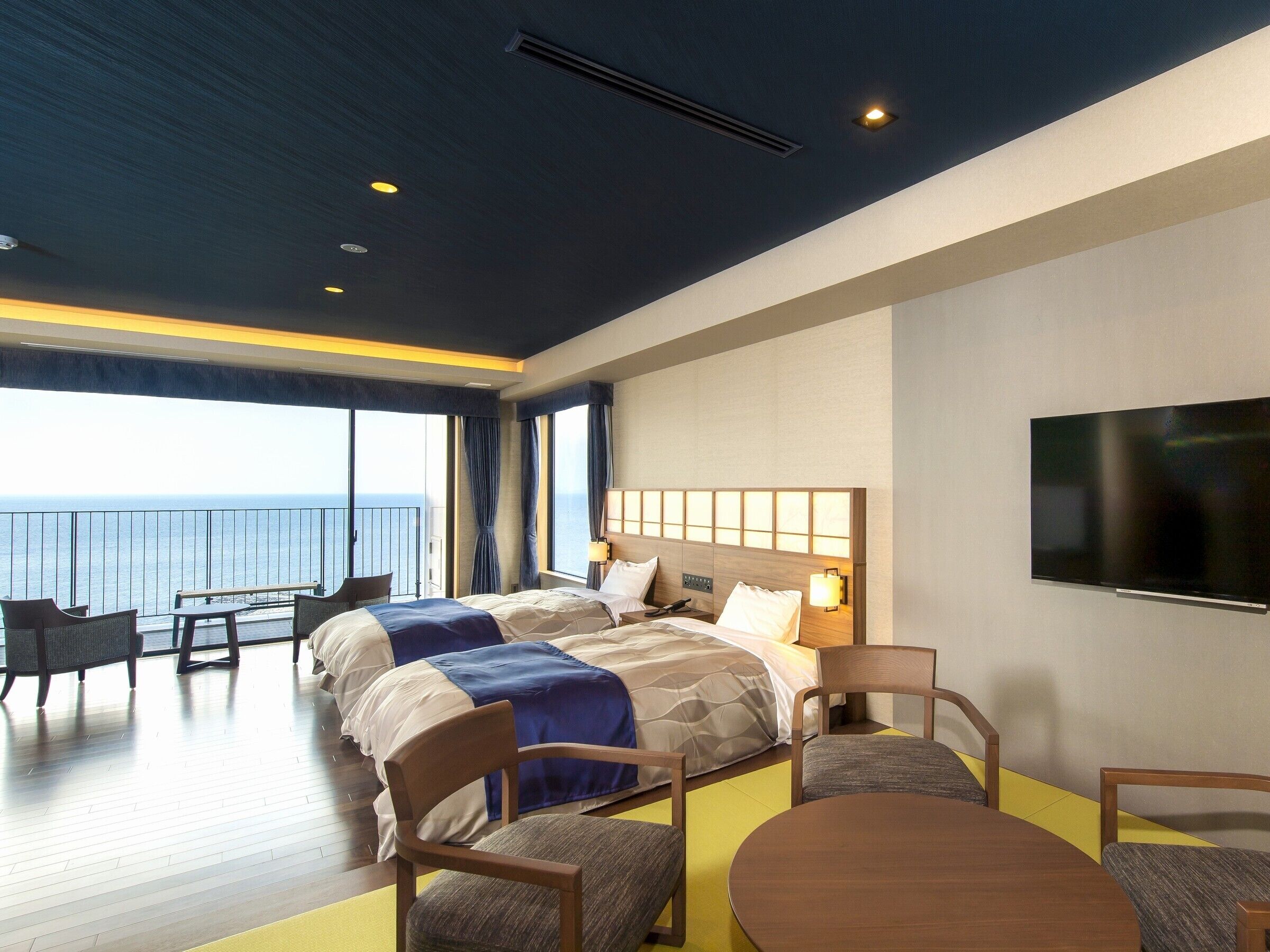 Une chambre d’hôtel avec un grand lit, une télévision, un balcon avec vue sur la mer et un coin repas.