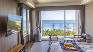 A hotel room with a large bed, a TV mounted on the wall, a balcony with a view of the sea, and a small table and chair set. - REX HOTELBeppu (Beppu)