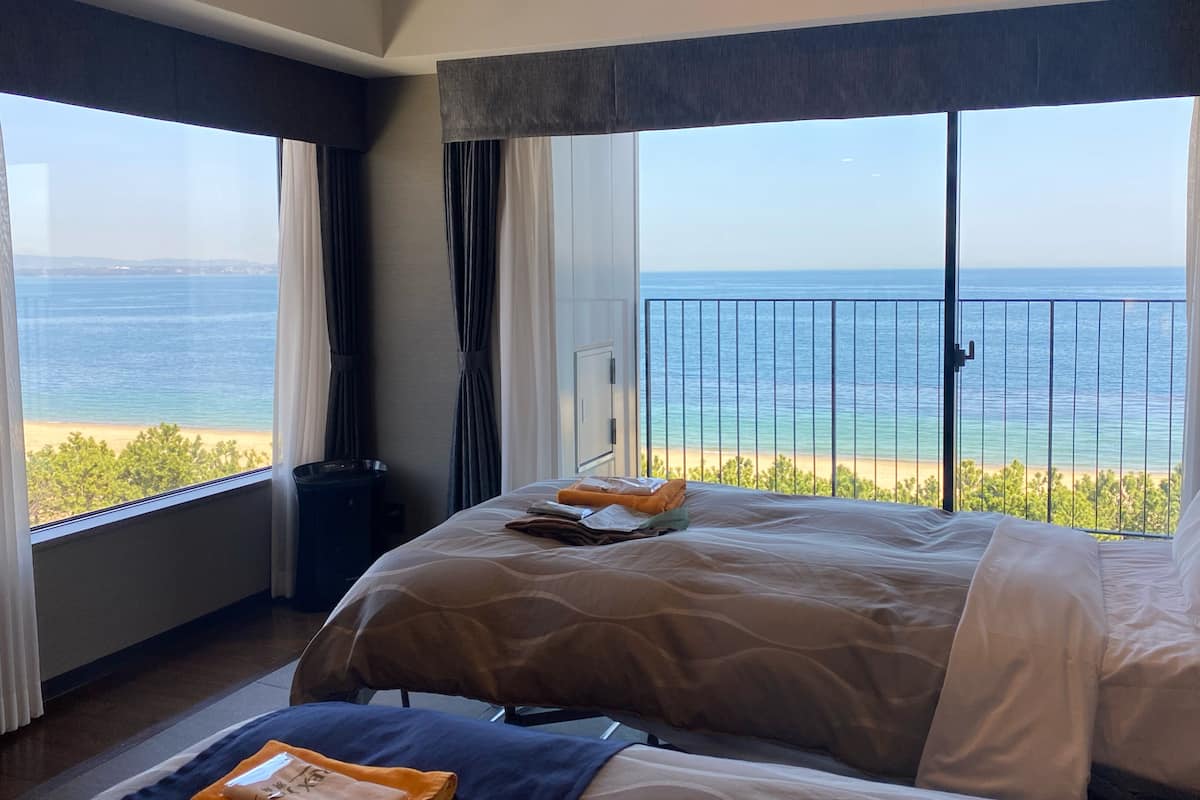 Ett hotellrum med en stor säng, utsikt över stranden och en balkong med ett räcke.