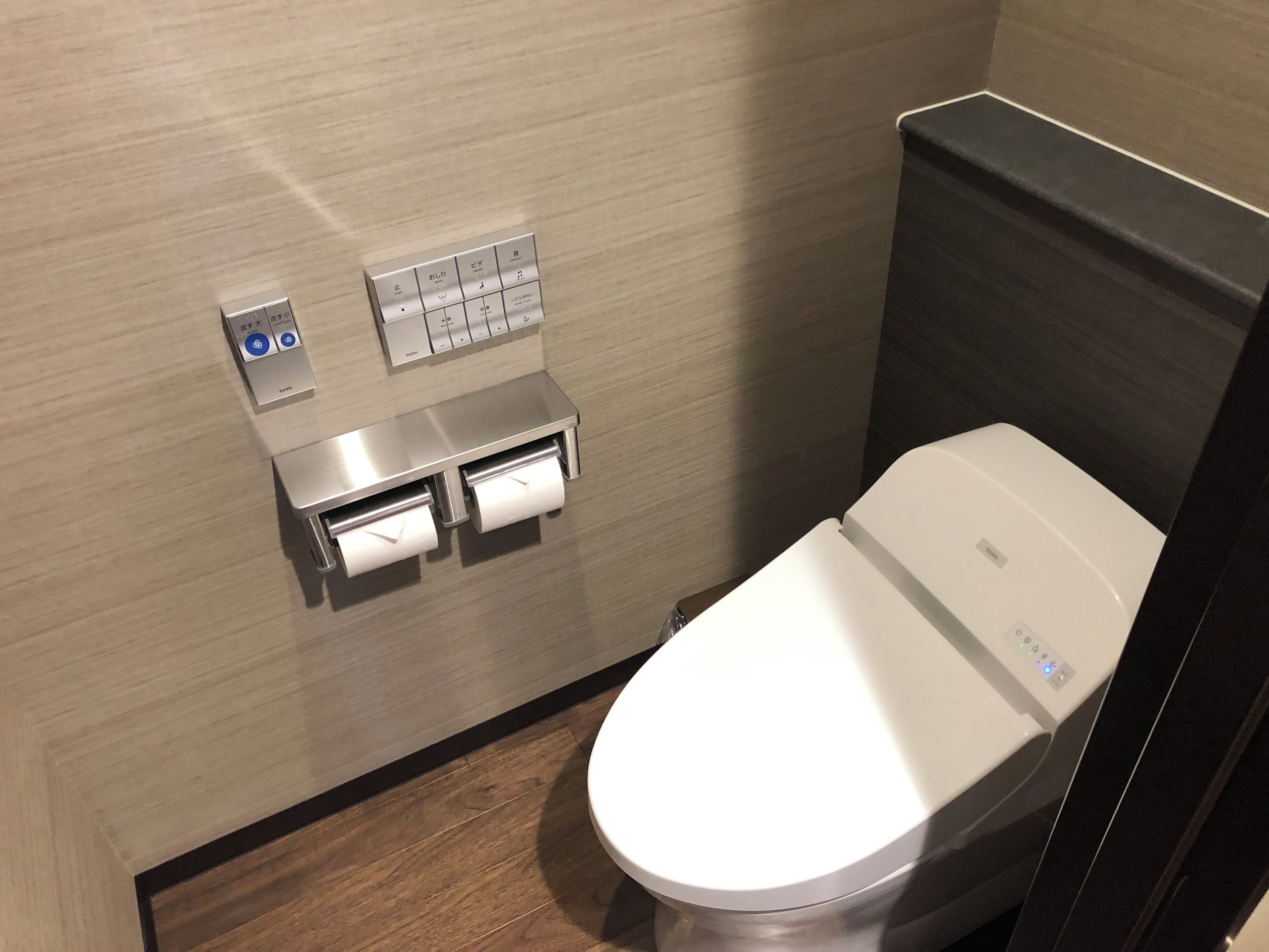 Une salle de bain moderne équipée de toilettes, d’un distributeur de papier toilette fixé au mur et d’un panneau de commande.