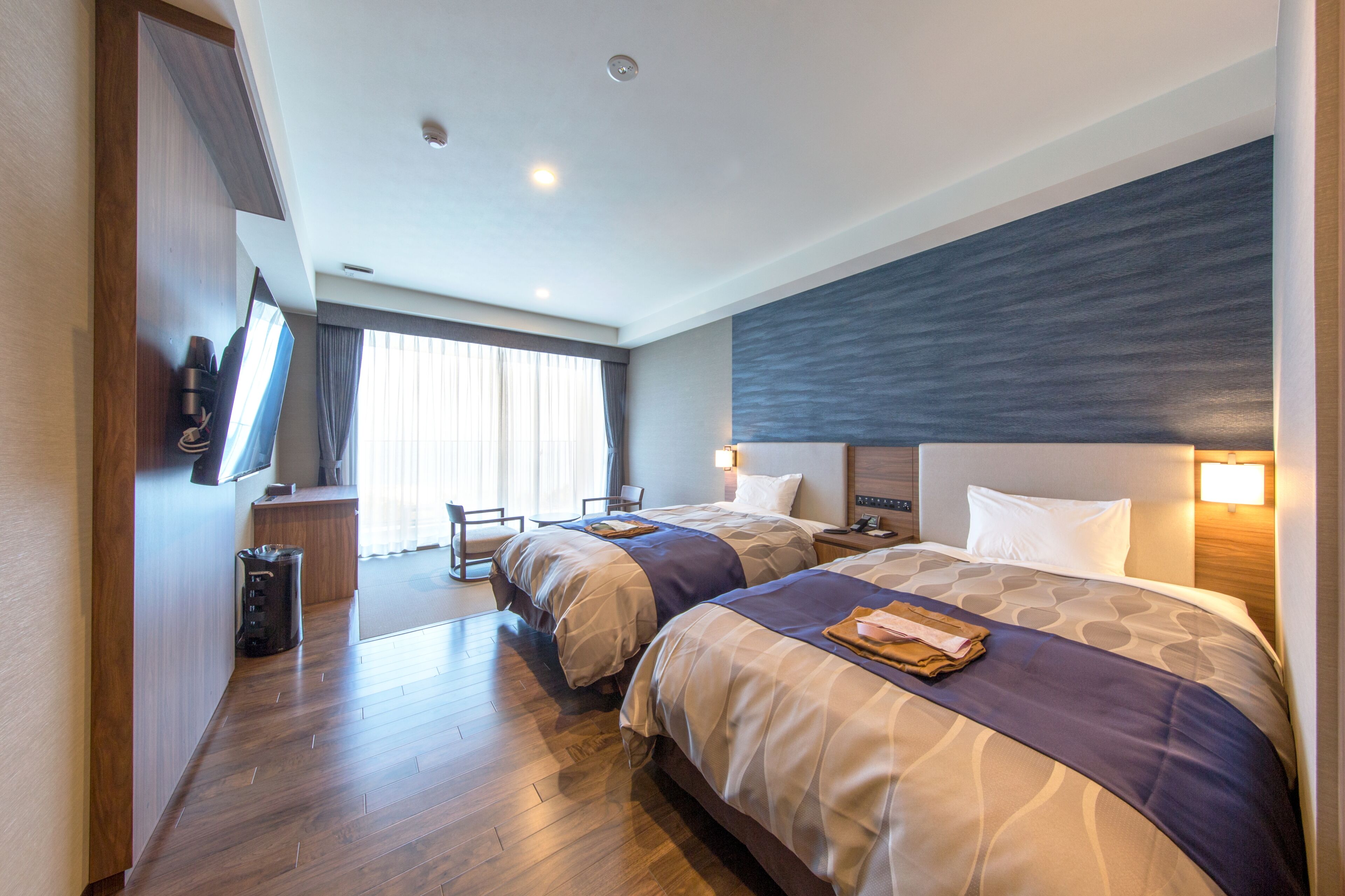 Habitación de hotel con dos camas, un escritorio, una silla y un televisor.