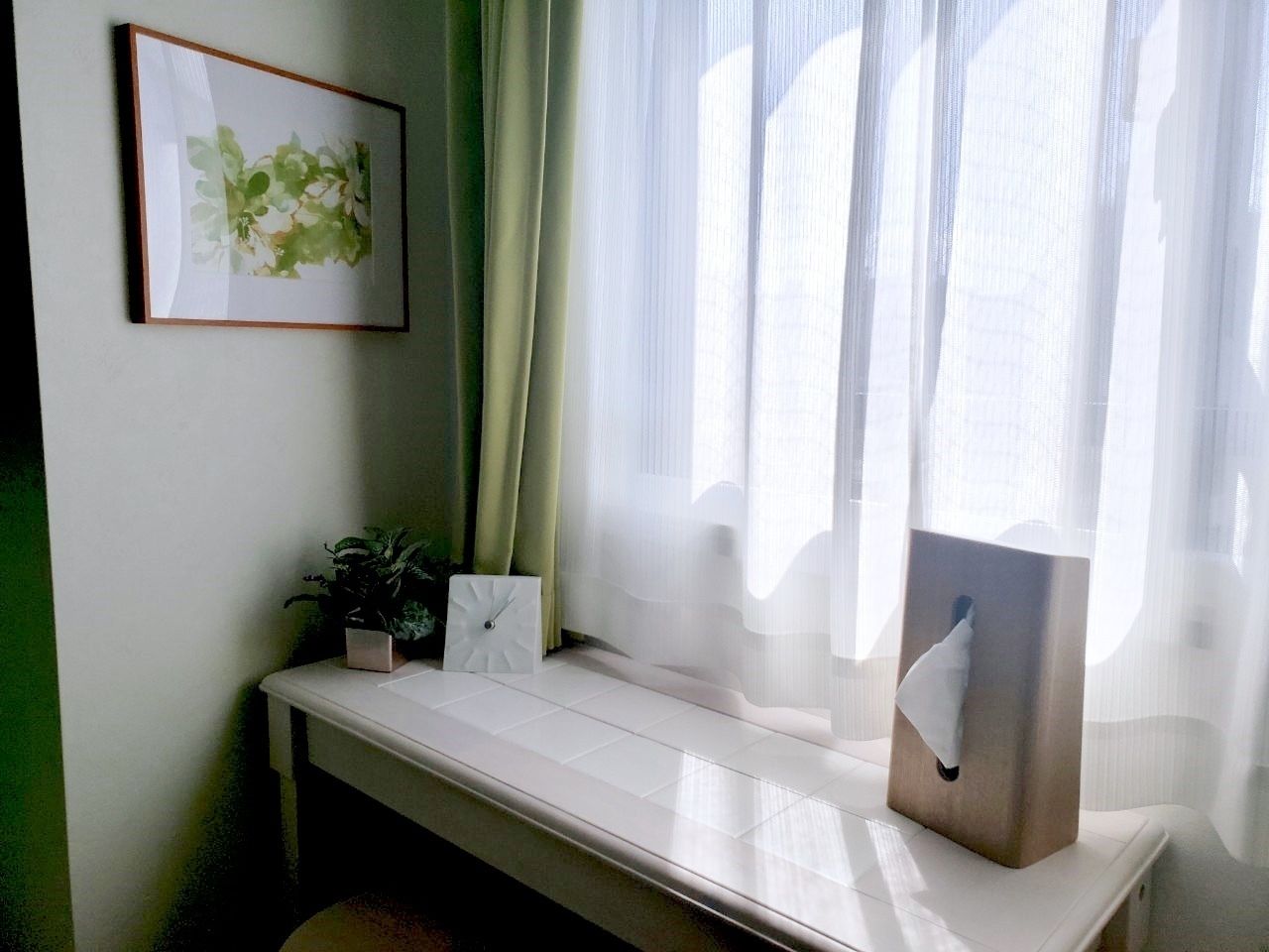Ein Zimmer mit einer weißen Bank, einem gerahmten Bild an der Wand, einem Blumentopf und einer Taschentuchbox.