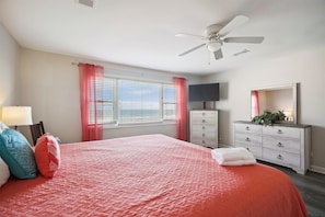 A bedroom with a large bed, a ceiling fan, a dresser, a TV, and a window with curtains. - Tropical Fun, Oceanfront Luxury Home in Cherry Grove with Private Outdoor Swimming Pool and Beautiful Ocean Front Views (NORTH MYRTLE BEACH)