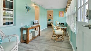 Una habitación con paredes color turquesa, una consola de madera, sillas de mimbre y una puerta con ventanal.