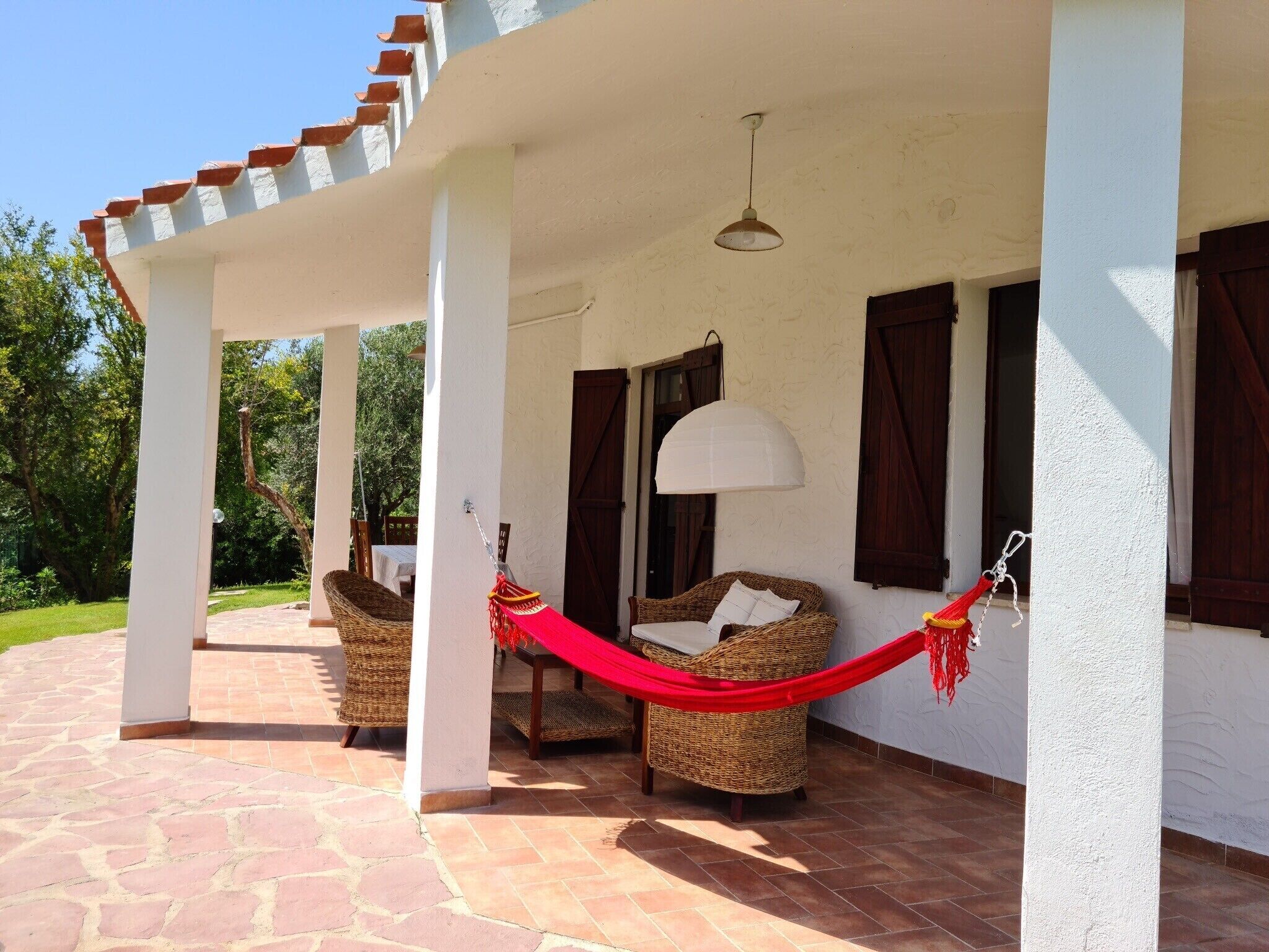 A covered outdoor seating area with wicker furniture and a red hammock.