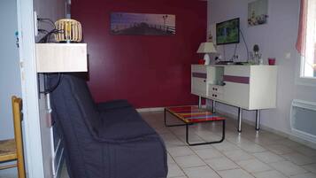 A room with a red wall, a white cabinet, a black sofa, a small table, and a television on the wall.