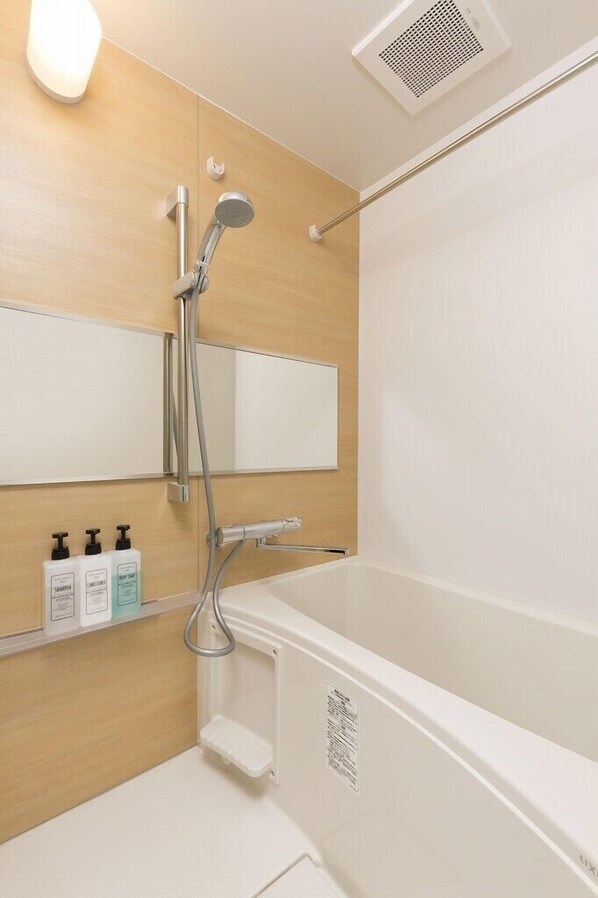 Une salle de bain moderne équipée d’une douche, d’un miroir et d’une étagère où sont rangés les articles de toilette.