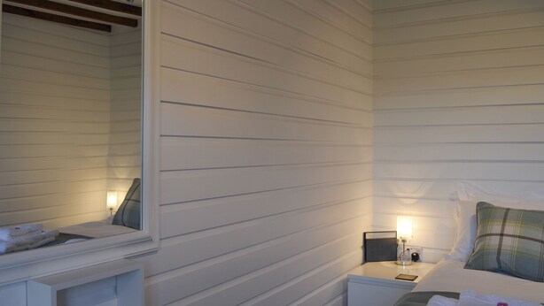 A bedroom with white paneled walls, a bed with a green and white pillow, a nightstand with a lamp, and a mirror above the dresser. - 1 bedroom accommodation in Borrowdale, near Keswick (Borrowdale, near Keswick)