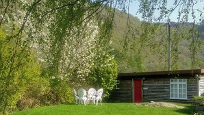 A rustic cabin with a red door, surrounded by a grassy area with white chairs and a small stream. - 1 bedroom accommodation in Borrowdale, near Keswick (Borrowdale, near Keswick)