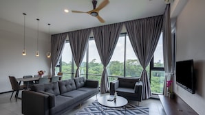 A modern living room with a sofa, armchairs, a coffee table, and a TV. There are curtains, a ceiling fan, and a dining area with chairs and a table. - Opus Residences (Kuala Lumpur)