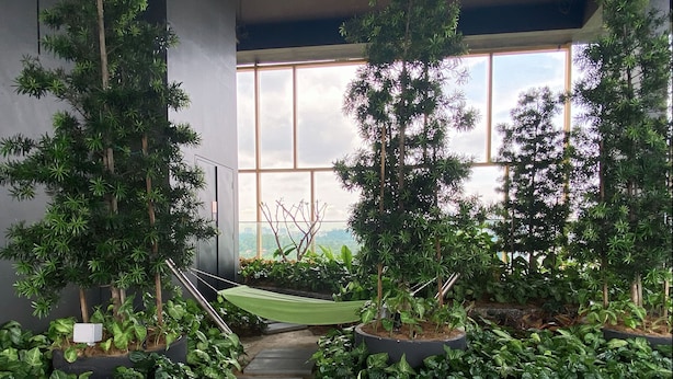 A staircase surrounded by lush greenery and potted plants, leading to a bright area with large windows. - Opus Residences (Kuala Lumpur)