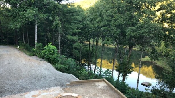 A patio with stone seating and a fire pit, surrounded by dense forest and a lake. - Exclusive private mountain and lake vacation in the Cohutta wilderness (Ellijay)
