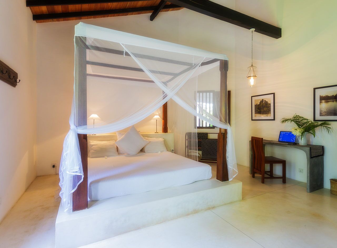 A bedroom with a four-poster bed, a desk with a computer, and a chair.