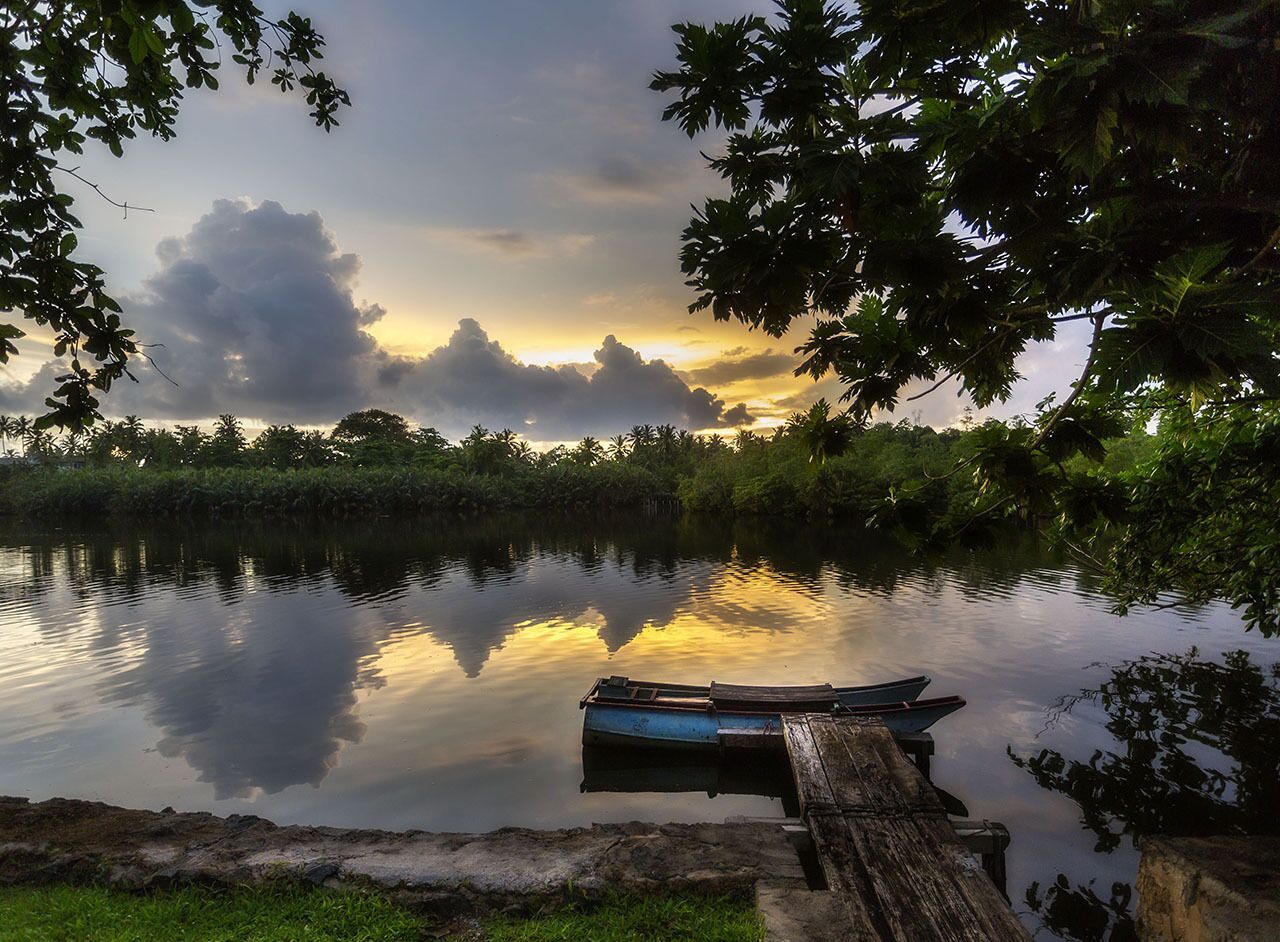 A calm lake with a wooden dock and a boat, surrounded by lush greenery and trees.