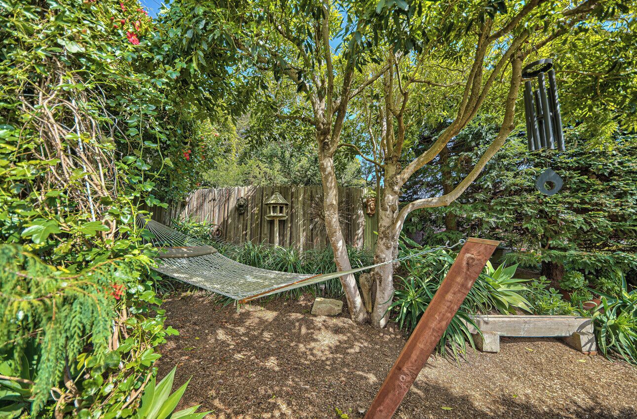 A hammock in a garden with dense foliage and a wooden bench.