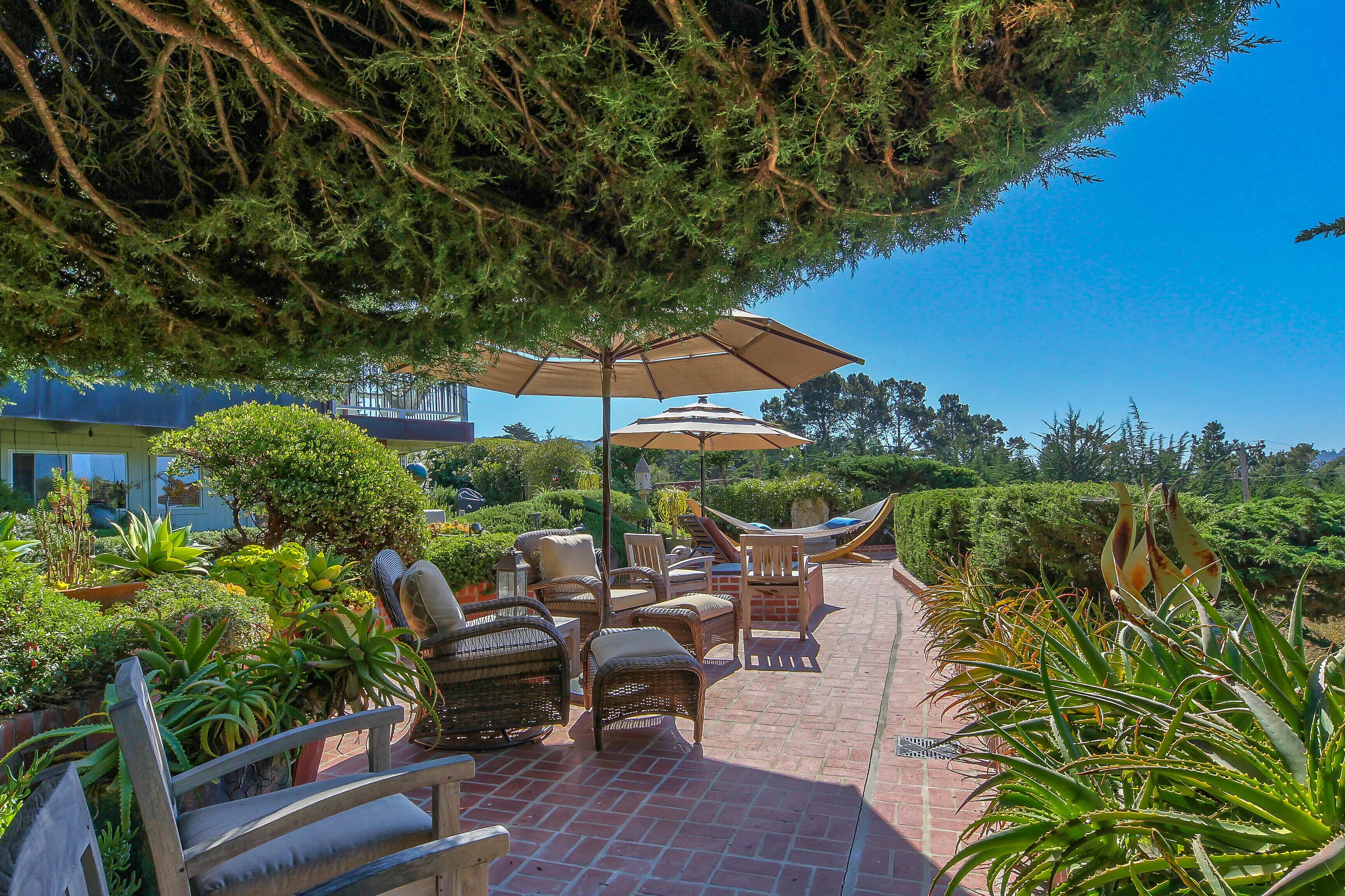 An outdoor patio with wicker furniture, umbrellas, and a variety of plants.
