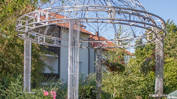 Un pabellón con techo de metal y cúpula, rodeado de follaje y flores.