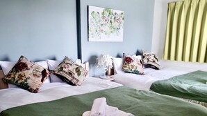 Ein Hotelzimmer mit zwei Betten, Bettwäsche in Grün und Weiß, Kissen mit floralem Muster, einem Wandbild und einem grünen Vorhang.