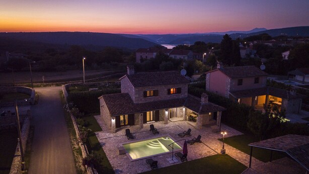 A stone house with a swimming pool, outdoor seating, and a view of the surrounding landscape at dusk. - VILLA SALVIA**** Rakalj  (Rakalj)