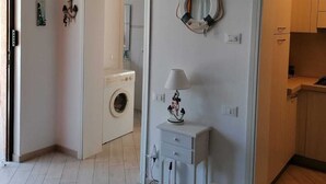A modern apartment with a washing machine, a small desk with a lamp, and a kitchen area. - PROMOZIONE-Appartamento ristrutturato a 30 mt dal mare (Follonica)