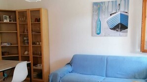 A living room with a blue sofa, a wooden cabinet, a dining table with chairs, and a hanging light fixture. - PROMOZIONE-Appartamento ristrutturato a 30 mt dal mare (Follonica)