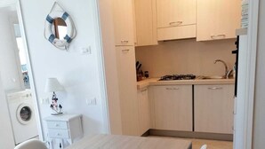 A modern kitchen with light wood cabinets, a stove, and a sink. There is a dining area with a wooden table and chairs. - PROMOZIONE-Appartamento ristrutturato a 30 mt dal mare (Follonica)